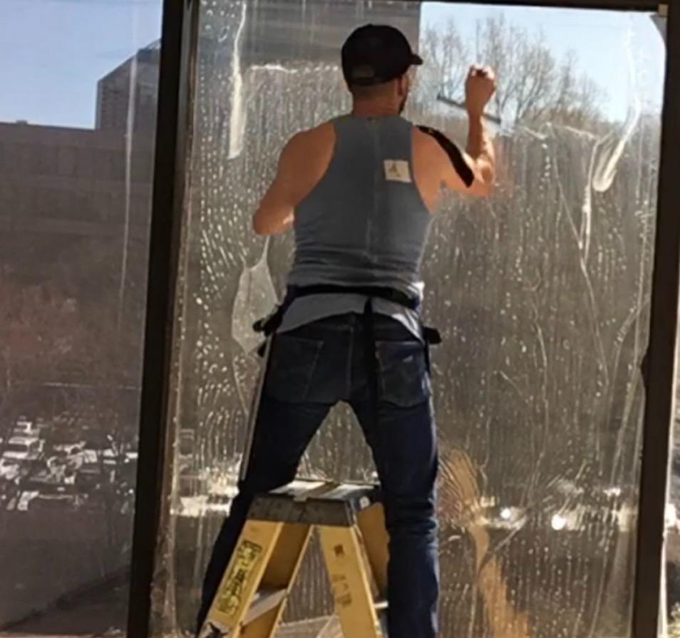 Technician applying window film to large glass panel on ladder outdoors