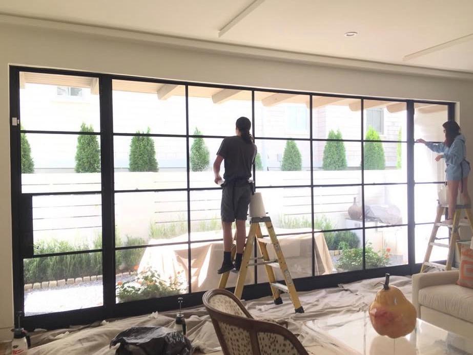 Two-person team installing film on steel-frame window wall in luxury home