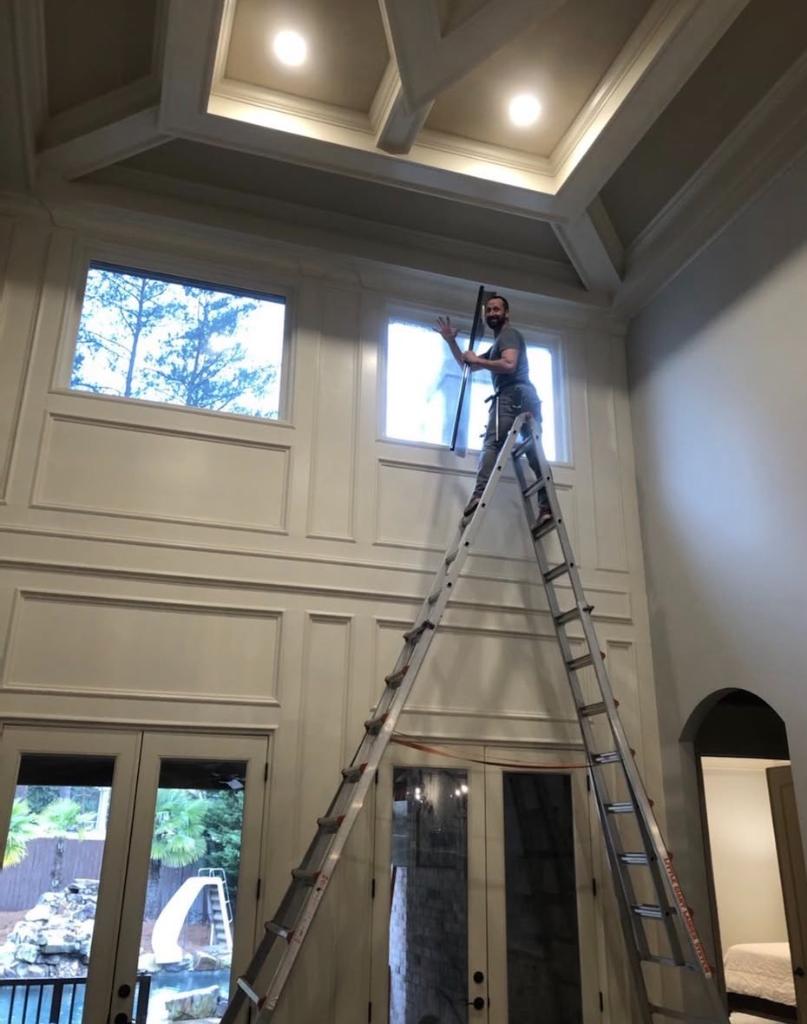 Joe from Sungate on tall ladder in luxury coffered-ceiling foyer installing window film