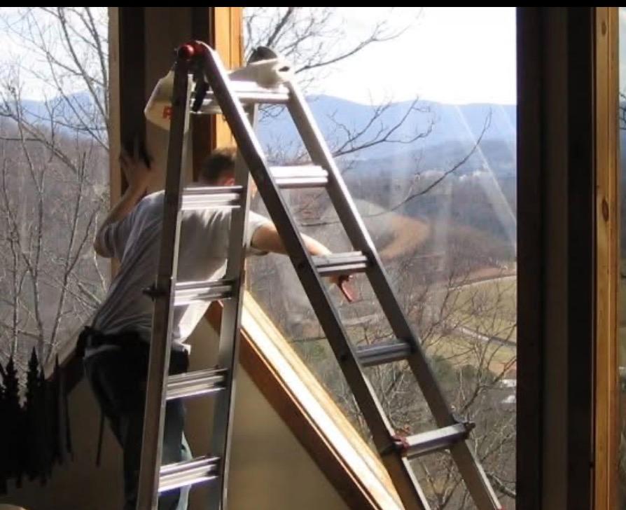 Technician on ladder applying film to large mountain-view windows