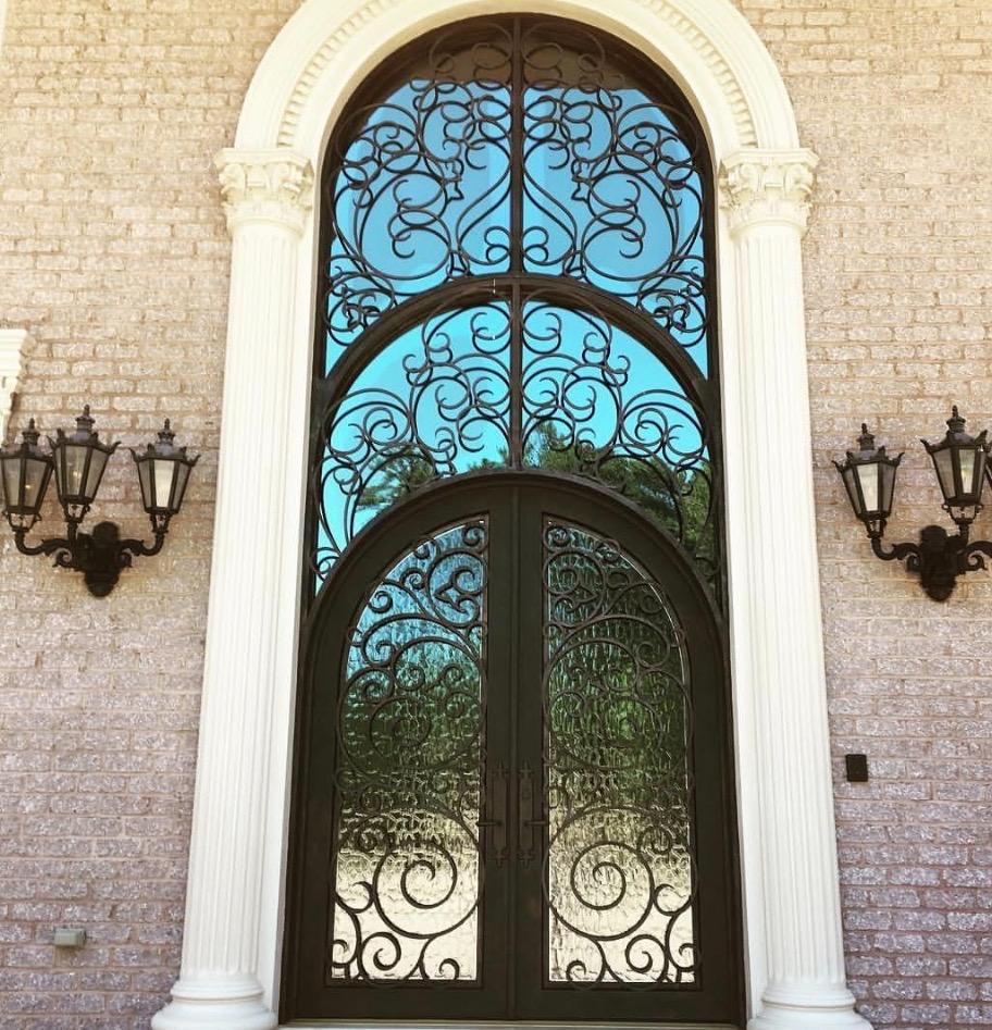 Grand arched iron double door with ornate scrollwork and tinted glass panels