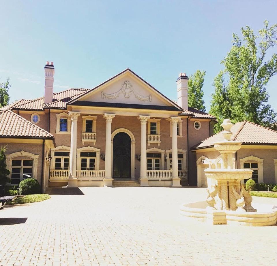 Luxury estate exterior with columns, fountain, and tinted windows