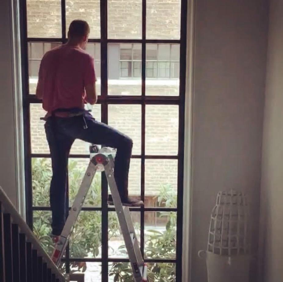 Installer on ladder applying film to tall black steel-frame grid window on staircase